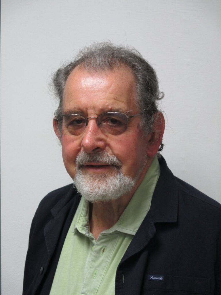 A picture of Robin Welch, author, wearing glasses, a black jacket and light green shirt.