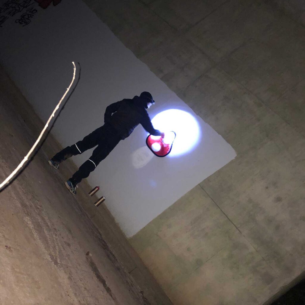 A person graffities a toadstool onto a wall at night.