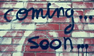 Coming soon written in graffiti on a wall.