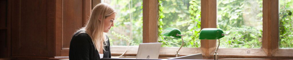 Student using a laptop by a window.